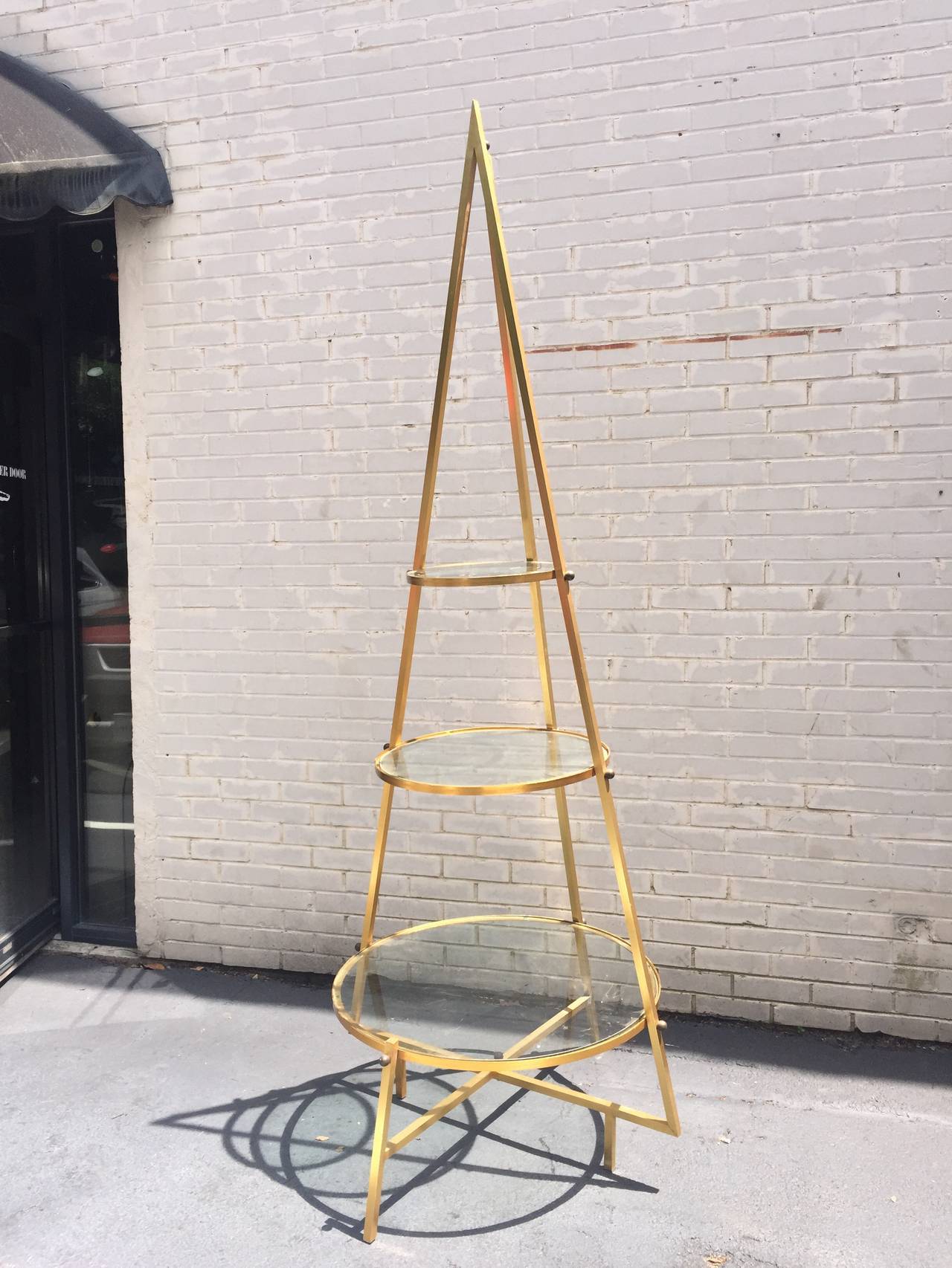Exceptional Mid-Century sculptural pyramid etagere display shelf. This unique design in comprised of a brass tone aluminum frame with three glass shelves. Very solid and well made great for displaying your favorite objects.