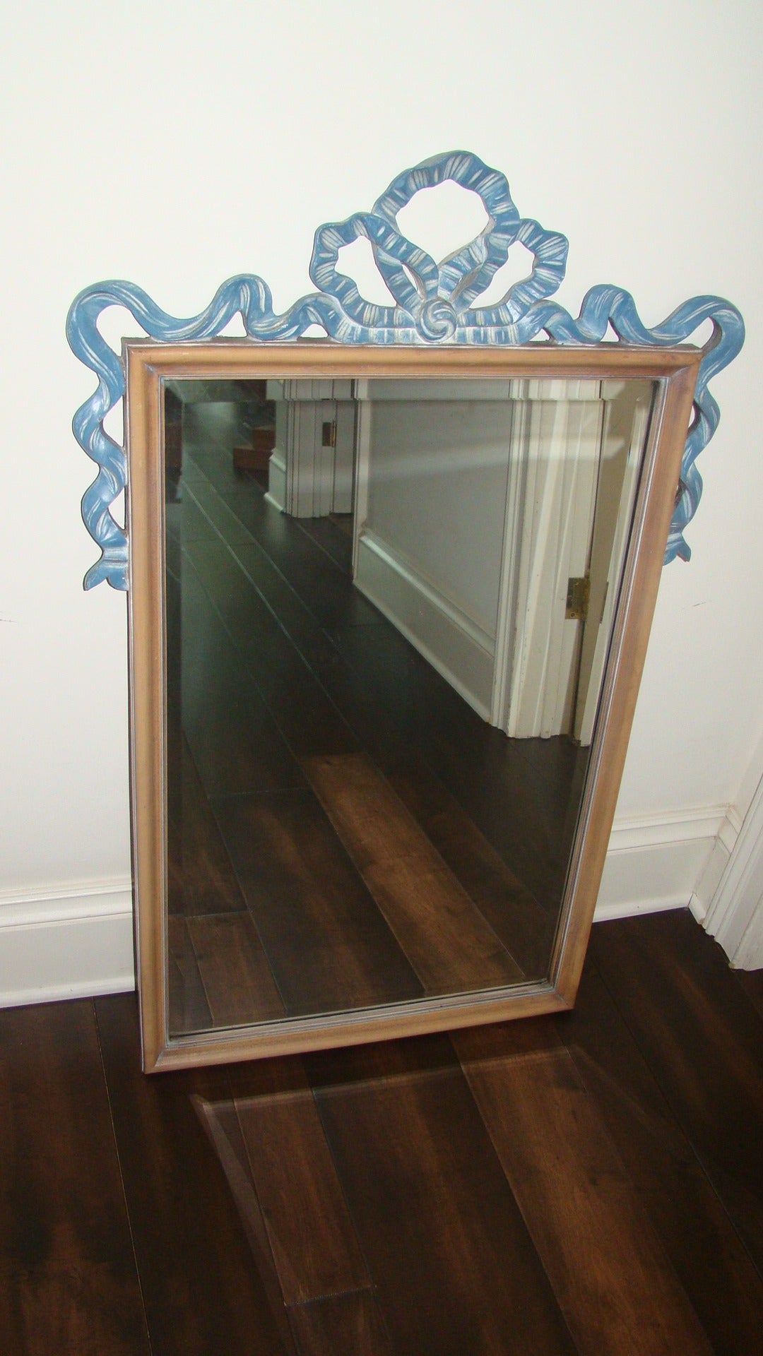 Glamorous Mid-Century sculptural wood ribbon wall hanging mirror in the manner of Dorothy Draper or Tommi Parzinger. The mirror is comprised of a wood frame with blue ribbon design along the top. The mirror has a bevel on the inside boarder. Truly a