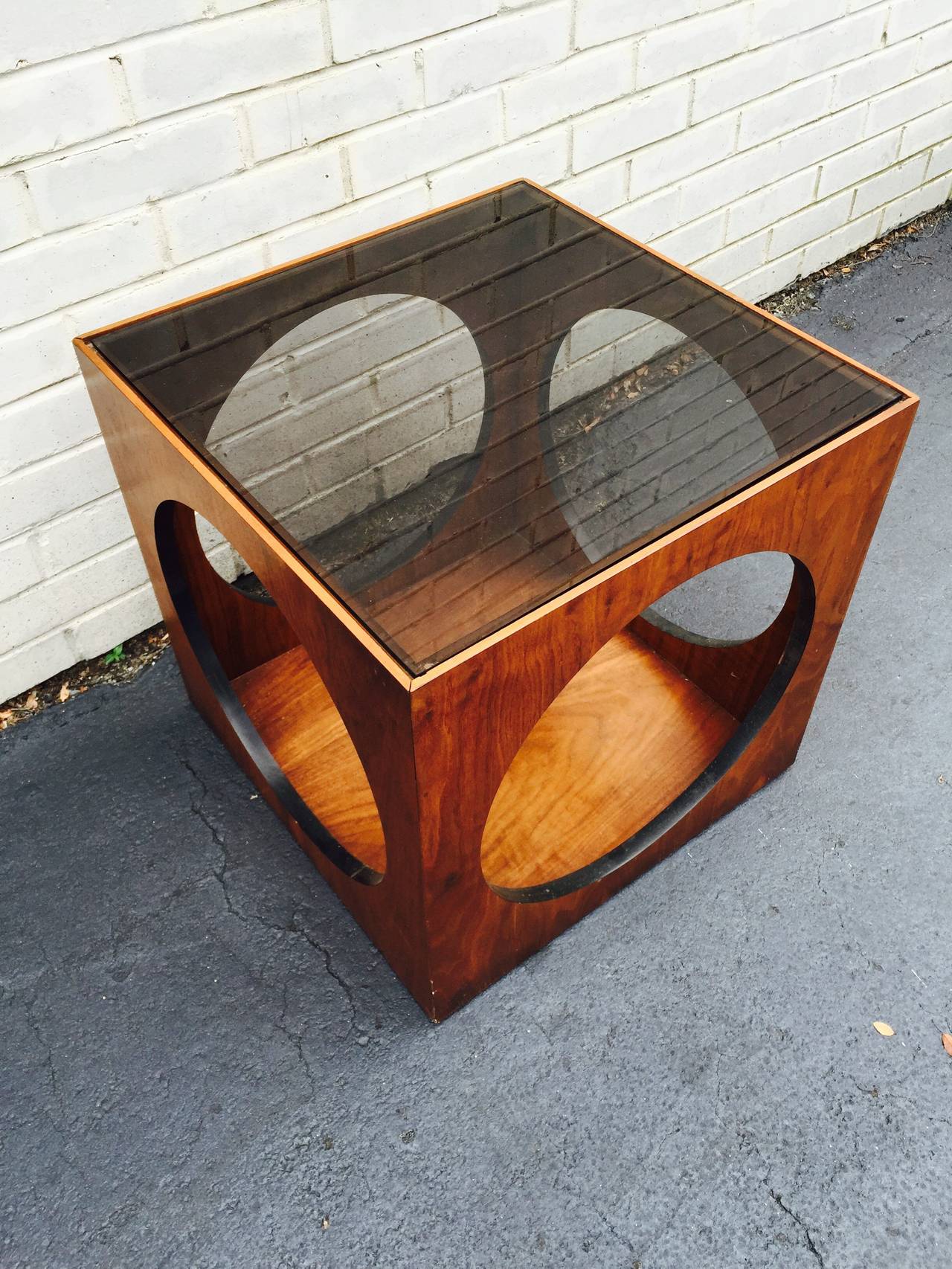 Terrific Mid-Century sculptural cube table by Lane. This interesting design is comprised of a walnut wood cube with circular cut-out on each side and tinted glass top. Great to display items inside and in top.
