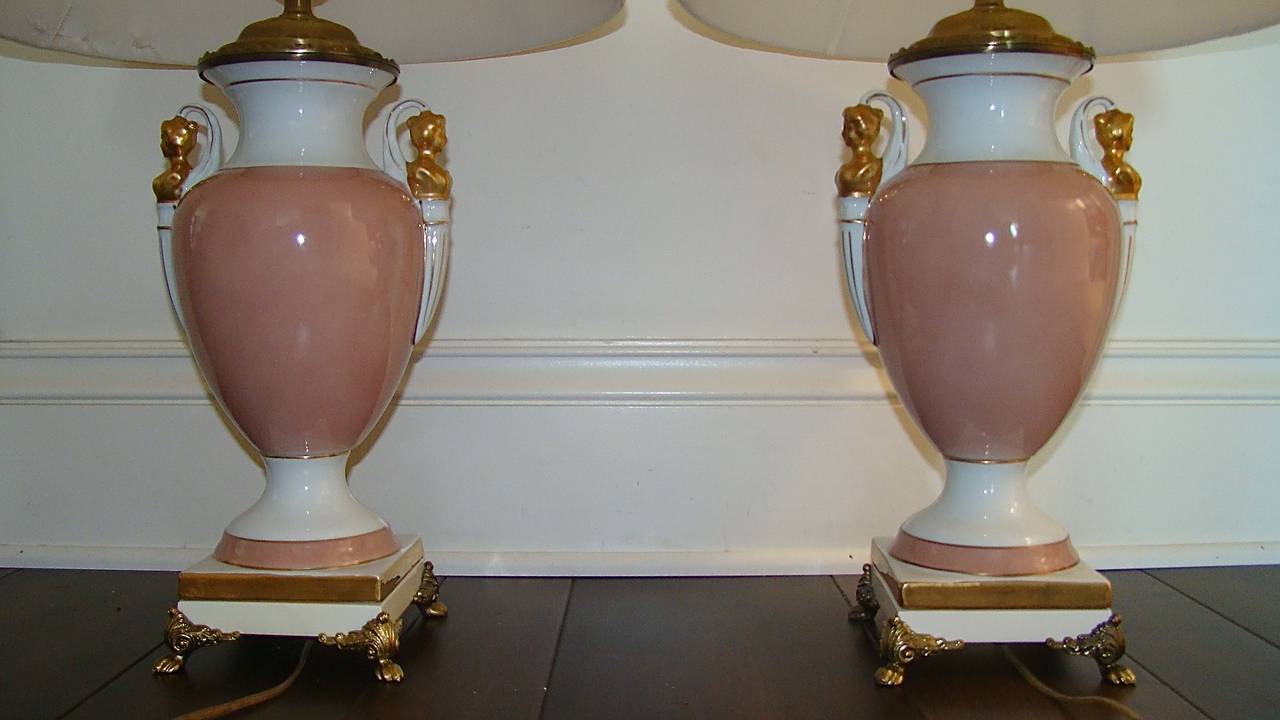 Beautiful pair of Ceramic Table Lamps by Paul Hanson. Each is comprised of a pink and white porcelain with gold neoclassical details and brass feet. Complete with matching finials. Shades not included . Truly a beautiful pair of lamps in person!