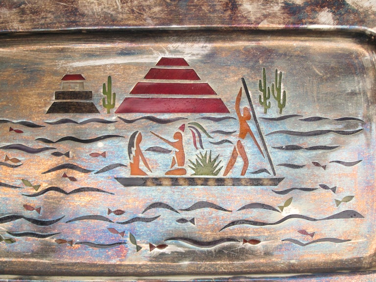 A beautifully crafted silver plated tray with the depiction - done in ‘pluma azteca’ - of a pre-colonial view of Teotihuacan, now Mexico City, when waterways dissected the land around the Aztec kingdom, dominated by its pyramids. ‘Pluma Azteca” was