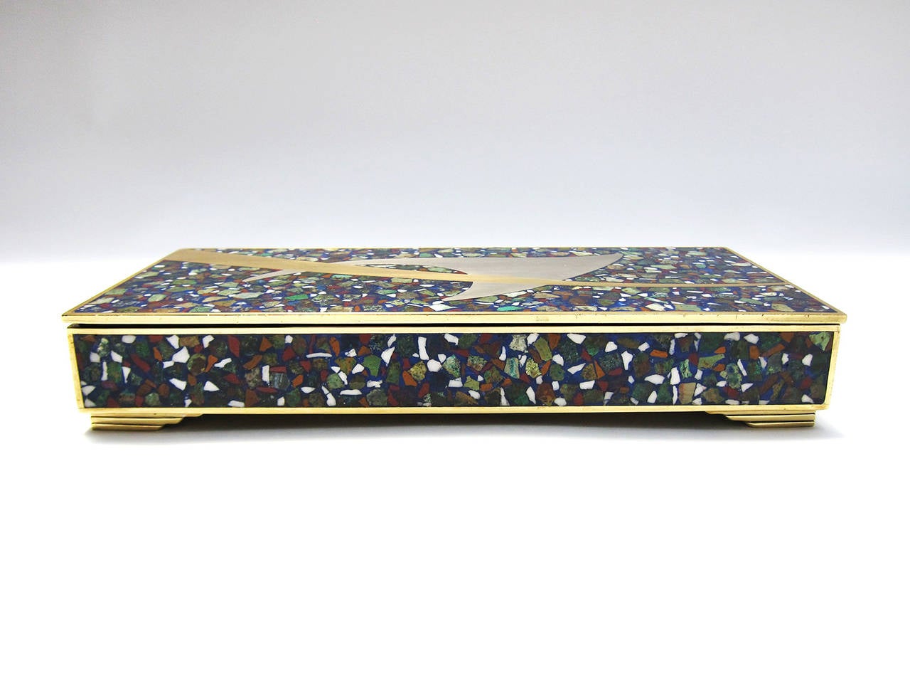 This unusual and elegant jewel box has a frame of brass with stone ‘confetti’ of crizacola, jasper y azur-malachite which are inlaid into a base of stone ‘dust’, possibly blue agate or lapisazuli. Breaking this background is a flash of brass and