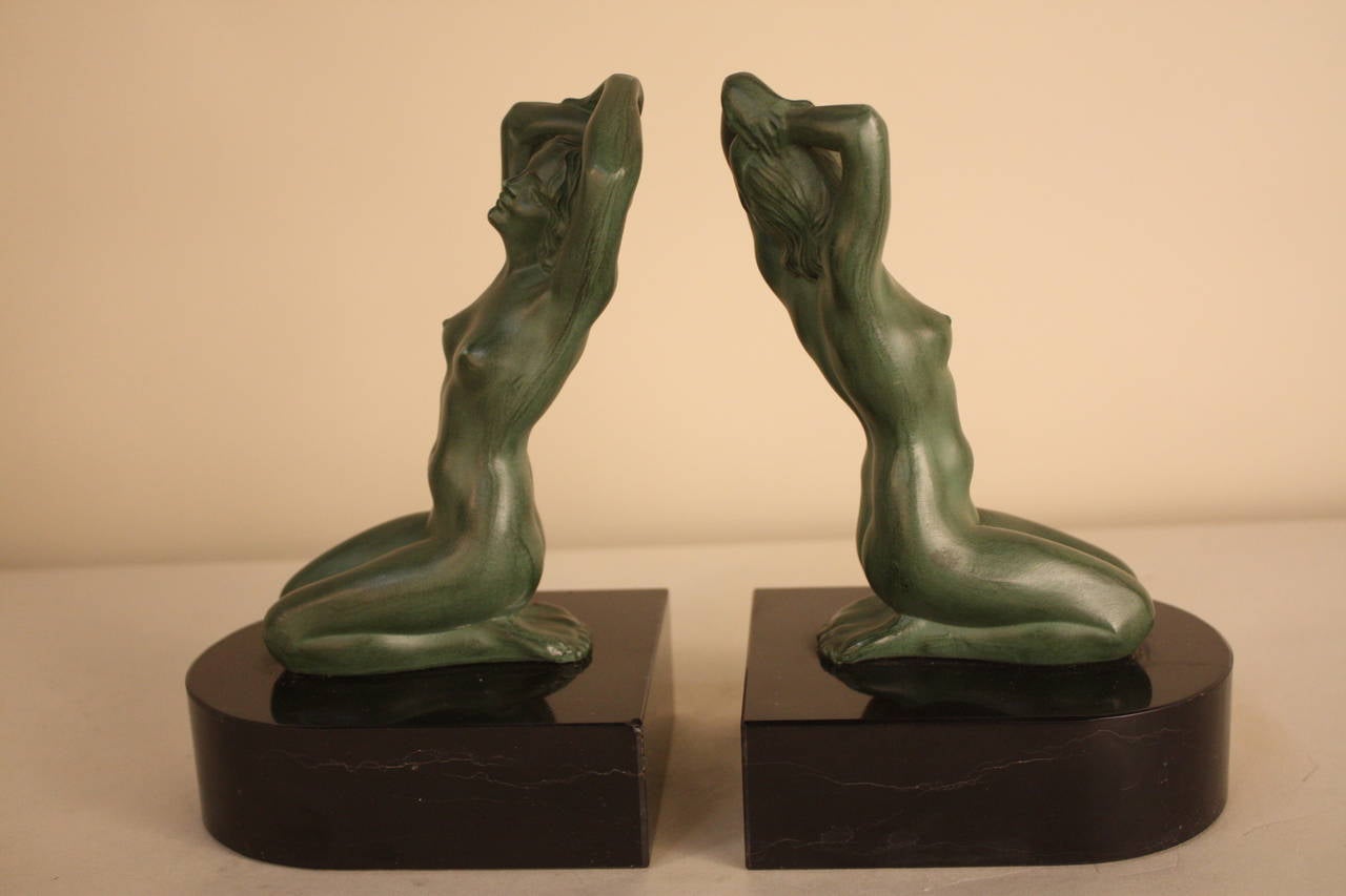 A pair of French Art Deco, green patina and black marble bookends with kneeling nudes holding her hair.