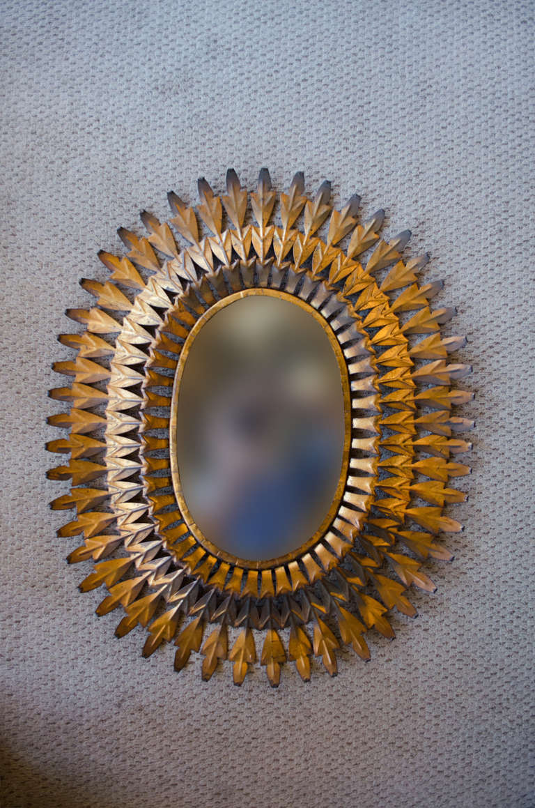 A fantastic wall mirror. Artisanally handcrafted in Spain, this mirror features an elegant oval sunburst style design made of gilded metal. Absolutely beautiful.