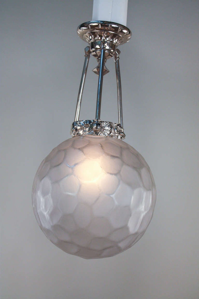 Made by world renowned French designers Genet & Michon, this elegant light fixture features a thick spherical frosted glass shade. An ornately decorated nickel on bronze body gives this piece a classic Art Deco look.