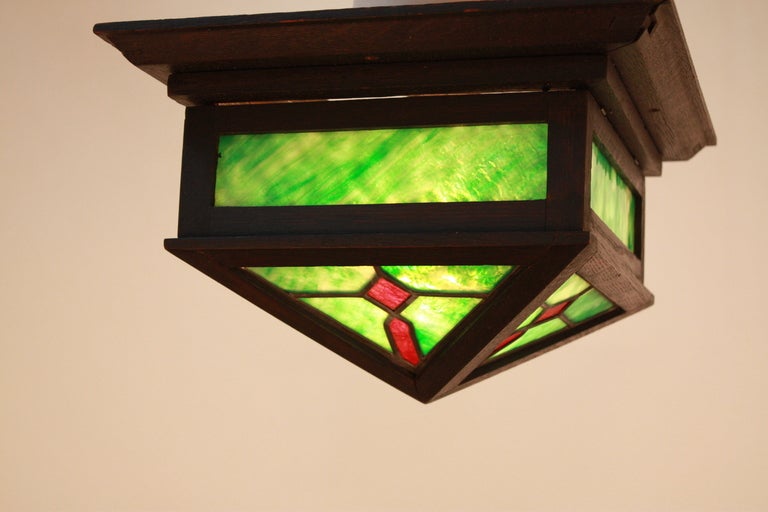 AMERICAN GREEN AND RED STAINED GLASS WITH WOOD FRAMING MISSION / ARTS & CRAFTS CEILING FIXTURE . THIS LIGHT HAS SINGLE LIGHT UP 200 WATTS BULB. WE HAVE A PAIR BUT ARE SOLD INDIVIDUALLY .