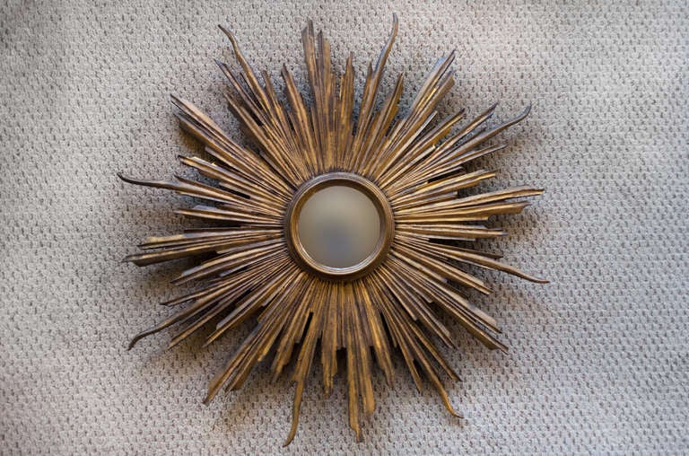 A beautiful hand carved mirror. Originally made in Spain, this wooden mirror features a classic Art Deco sunburst design and convex glass.