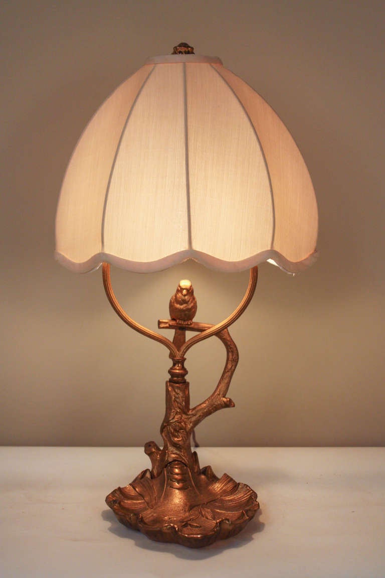 This elegant table lamp is made of beautiful bronze, and depicts a small bird perched on a tree branch. Filled with stunning detail work, this fantastic lamp is topped off with a custom made oval shade.