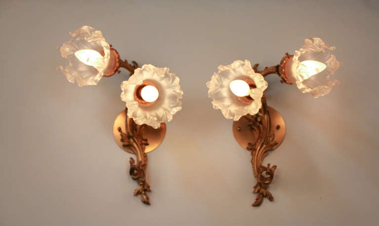 An beautiful pair of wall sconces. Masterfully crafted in France during the early 1900's, these wonderful sconces are heavily Art Nouveau influenced. Made of ornately detailed solid bronze, these double light sconces are topped off with elegant acid