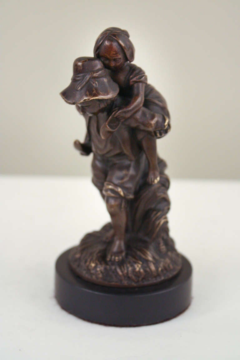 Masterfully crafted in France during the early 20th century, this beautiful statue is a true work of art. Made of solid bronze and a black lacquer over bronze base, the statue depicts one sibling, a boy, carrying his sister.