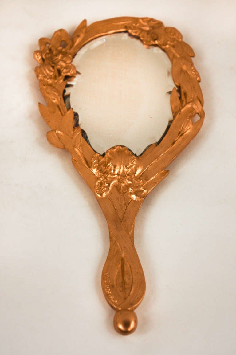 Masterfully crafted in France during the early 20th century, this hand mirror is truly timeless. Made of beautiful bronze doré; this mirror features beveled glass and an elegant organically-inspired design characteristic of Art Nouveau. This piece