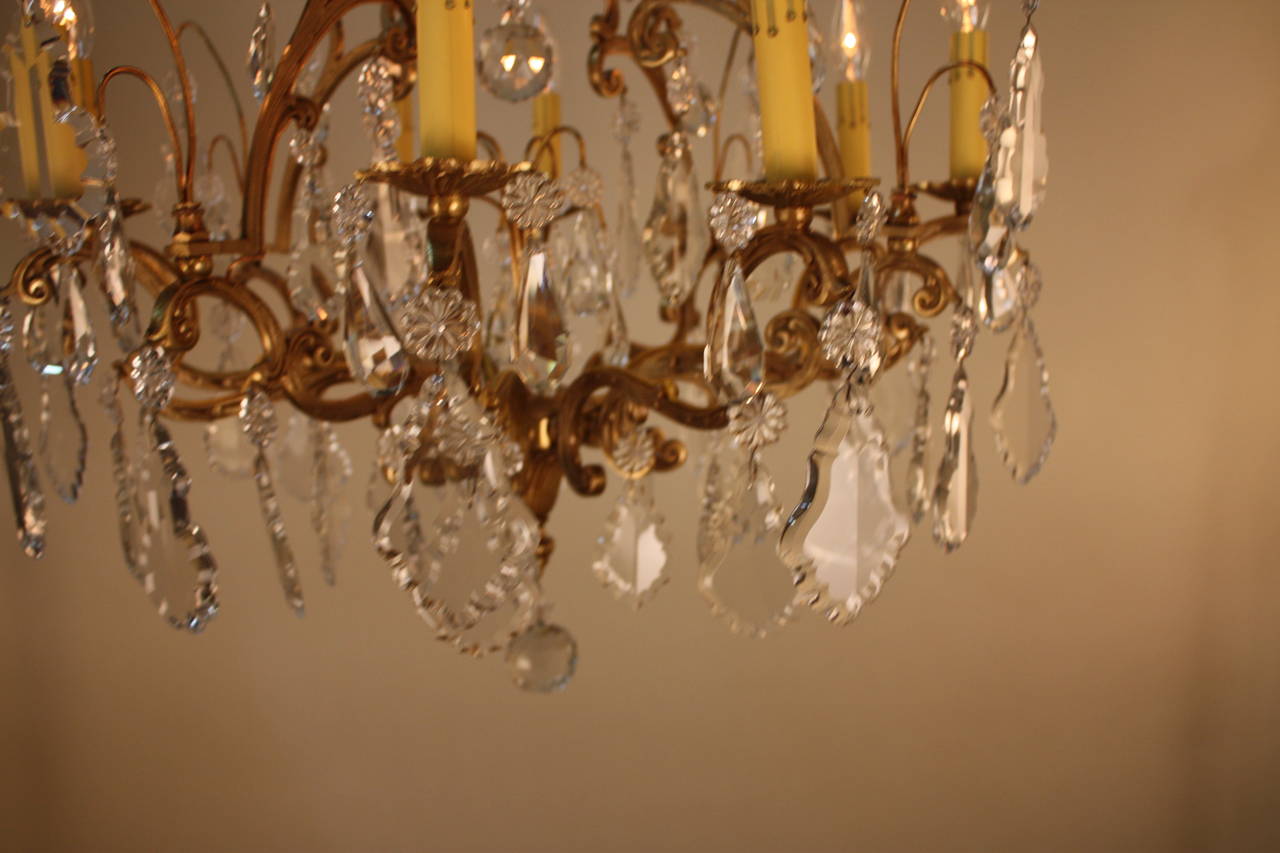 Made in France 1930s, this stunning chandelier is adorned with dozens of ornate crystals and elegant bronze. The chandelier features eight lights which beautifully illuminate the dangling crystals with a Classic elegance.