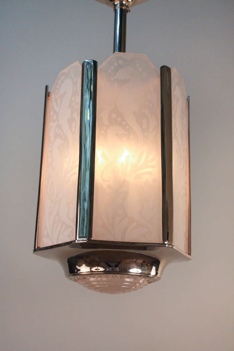 A classic Art Deco fixture with a unique touch, this lantern style chandelier is absolutely superb. Crafted in France during the 1930's, this beautiful six light chandelier is made of classic nickel on bronze and features six acid cut class shades