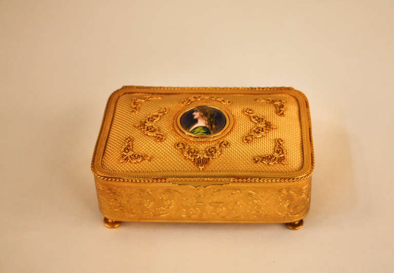 A beautifully made jewelry box from France. This fabulous jewelry box features ornately detailed gold-plated copper and a gorgeous enamel center medallion that depicts the portrait of a young woman.