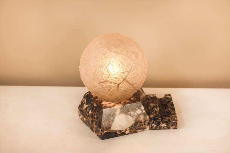 Made in France at the height of Art Deco, this beautiful table lamp is uniquely designed. This lamp features a heavy marble base is filled of a variety of gorgeous color, and is topped off with an elegantly designed glass globe shade.