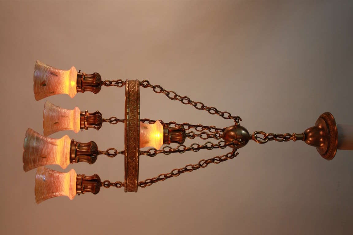 This is a fantastic American chandelier. Made of bronze, this chandelier features five signed Quezal art glass shades: decorated with glass thread on outside of each shade and brilliant gold inside that reflects beautiful warm colored light.