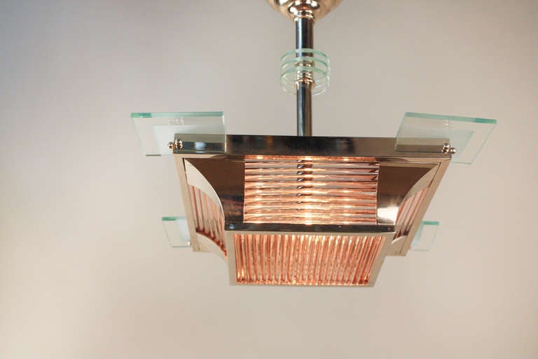 Elegantly designed by Atelier Petitot, this 1930's chandelier is a gorgeous example of modernist styled French Art Deco. 

Nickel on bronze hardware beautifully combines with clear glass accents. A solid glass rod design provides a warm peach