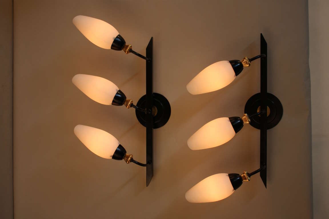 A pair of 1950s wall sconces, made by Arlus in France. These three-light fixtures feature a beautiful black enamel and brass design.