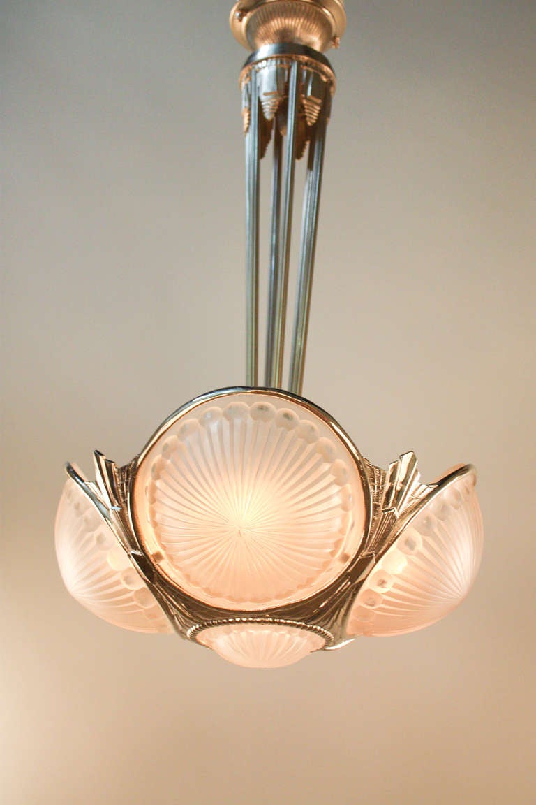 This French 1930s Art Deco chandelier features five glass panels and four lights. The glass panels have a beautiful geometric pattern, with lines reaching out from the center of the panel. It is framed with elegant nickel on bronze with a similar