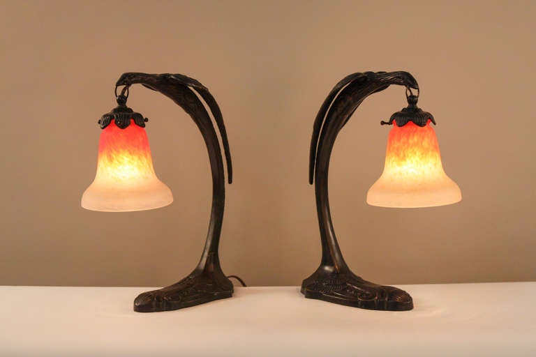 A fantastic pair of bronze table lamps. Resembling the legendary phoenix, these lamps feature a stunning modern design with signed Schneider glass shades.