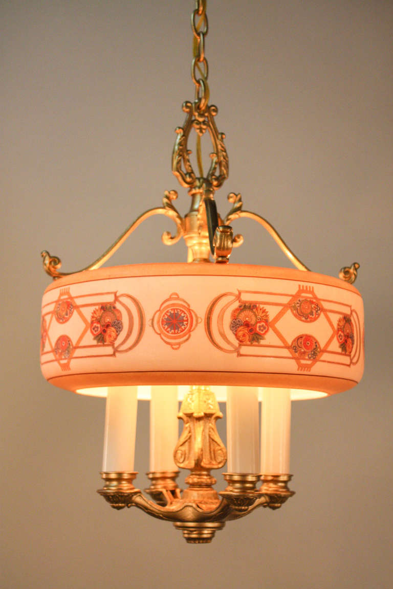 Featuring a brush-painted glass shade, this American 1930s chandelier holds four candle lights. The glass shade is multicolored, painted in a fantastic geometric pattern (see detail image). The metalwork has a nice design to it as well, that