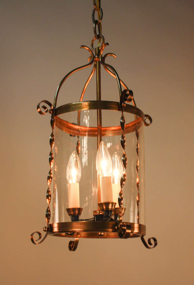 This beautiful piece is a three light 1950's bronze hanging lantern with a single slender glass cylinder shade. The outside bronze work is twisted in a simple, gorgeous design, highlighting the beauty of this French lantern.