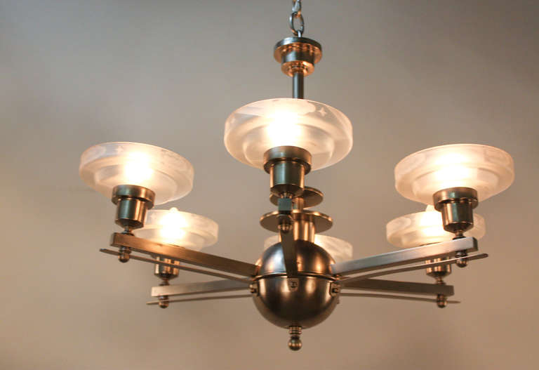 Crafted in France during the 1930s, this chandelier is a true Art Deco classic. The chandelier is made of gorgeous nickel on bronze and features etched glass shades. The glass shades have a beautiful leveled shape to them, and are finished with