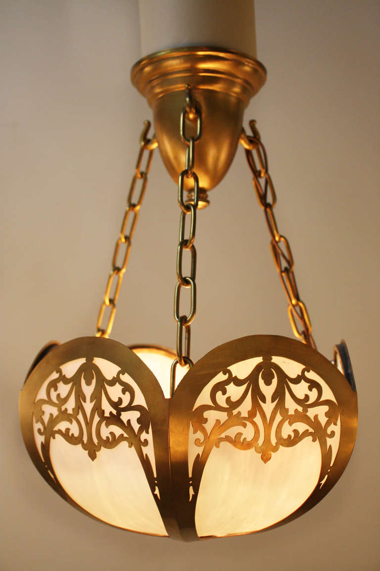 This 1920's American chandelier is made of gorgeous white stained glass and brass. The brass has a beautifully cut design, and the chandelier is suspended from the ceiling by three adjustable brass chains. This chandelier has a single but powerful
