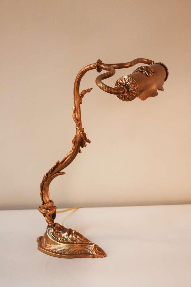 This timeless desk lamp features an adjustable arm and shade. Made of bronze,  this lamp features influences of the Art Nouveau style. The lamp's branch-like design is filled with masterfully crafted detail work: leaves wrap around the arm, and a