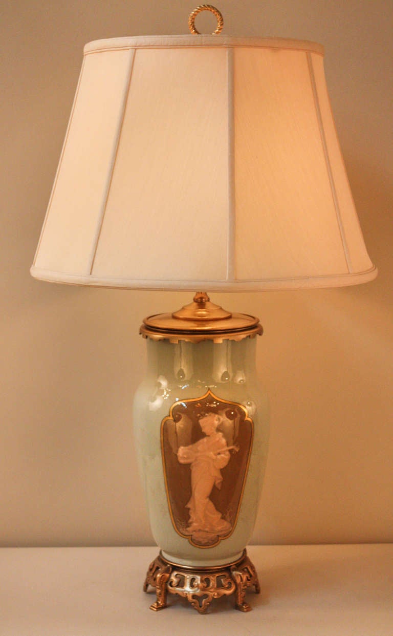 Masterfully crafted in 19th century France, this gorgeous table lamp depicts scenes of musical passion and the serenity of nature. 

Originally an oil lamp, this table lamp has been professionally electrified. Made of celadon, this piece combines