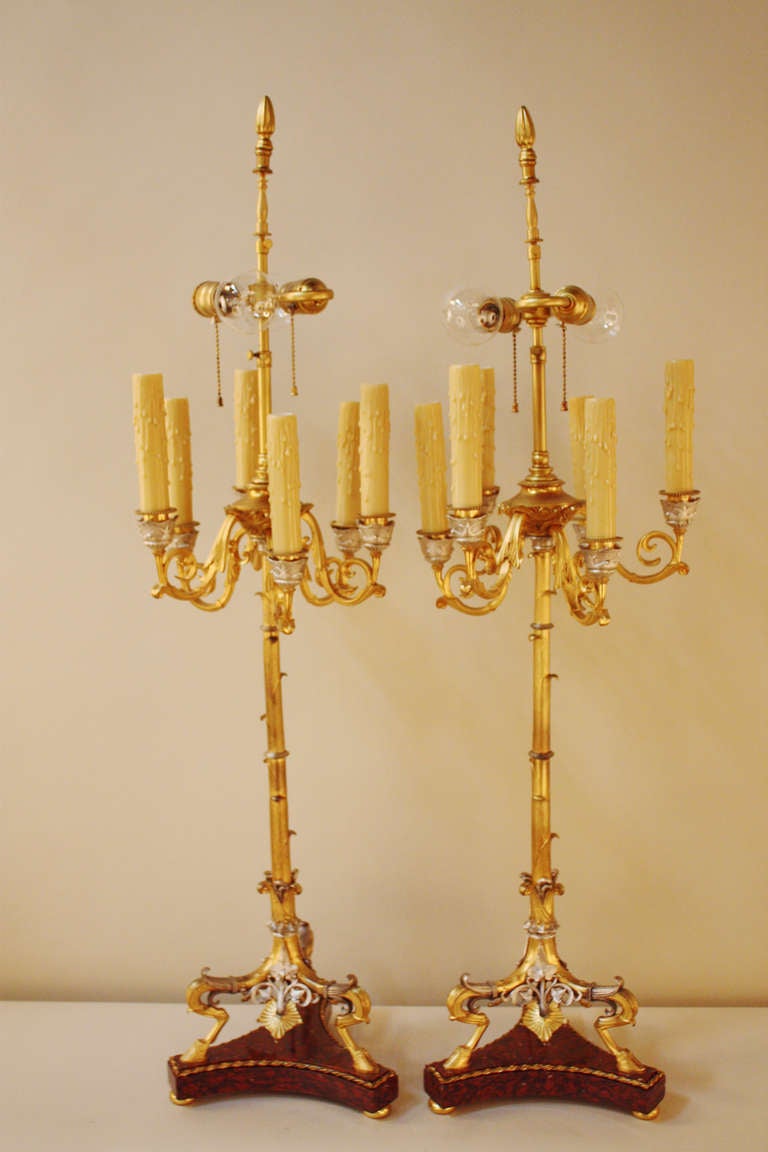 Crafted in France during the 1800s, these pieces originally served as candelabras. They have been professionally electrified as lamps for modern use. 

Dazzling in gold and silver over bronze, these Empire lamps feature stunning details from top