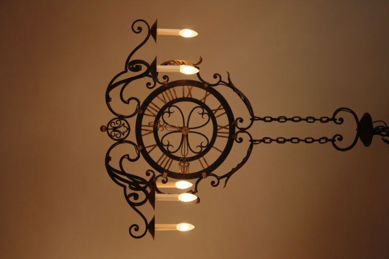 THIS 1930 CHANDELIER IS HAND FORGED WROUGHT IRON WITH CLOCK TYPE DESIGN IN THE CENTER IT HAS TOTAL OF 6 LIGHTS