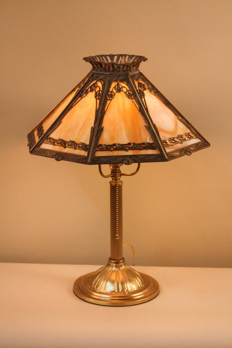 This 1920s American stained glass lamp has a classic style. Beautiful stained glass makes up the shade; accented by Art Nouveau-style brass and spelter detail work. 

This table lamp has a diameter of 14