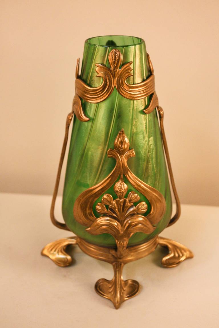 Made in Austria at during the early 1900s, this Art Nouveau vase is as beautiful today as it was a century ago. The vase's amazing iridescent green blown glass is wrapped in an elegantly designed bronze base. A truly remarkable piece of art.