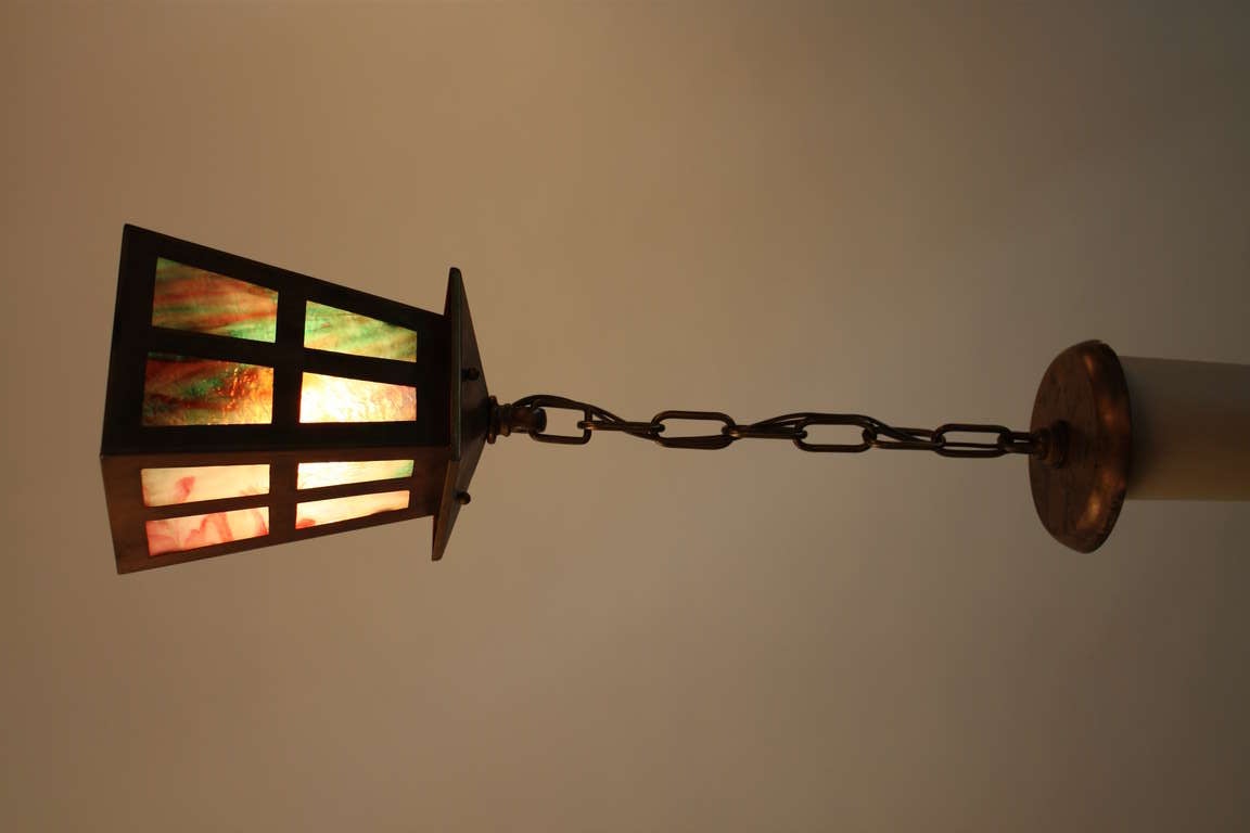 This stunning pendant light is a beautiful example of the American Arts & Crafts movement. A single light fixture, this piece is decorated with panes of multicolored stained glass.