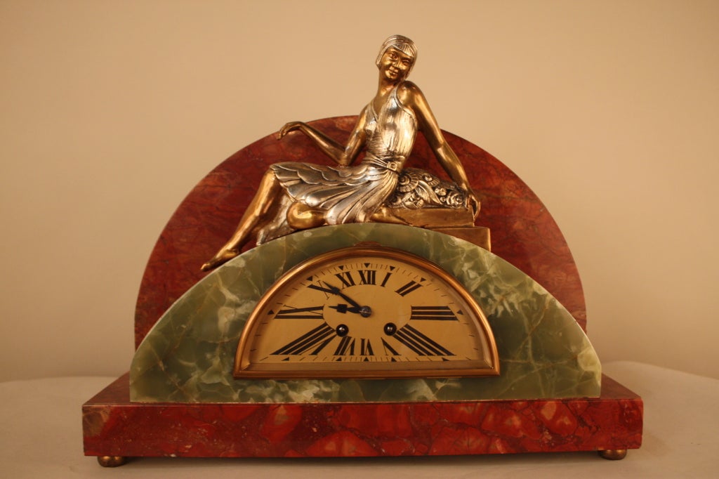 This stunning Art Deco clock is made of green onyx and marble. A beautiful work of art; this piece features a bronze and silver-plated figure of a young woman seated atop the clock's mantel.