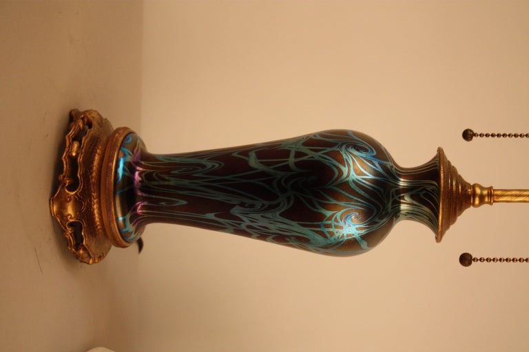 An extraordinary art glass lamp. Crafted from an purple iridescent vase with a brilliant turquoise coil design, this table lamp sits atop gilded metal base.