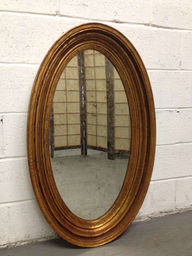 Pair of gold gilt oval mirrors with non-wood frames. Mirrors have a light smoked pattern. 