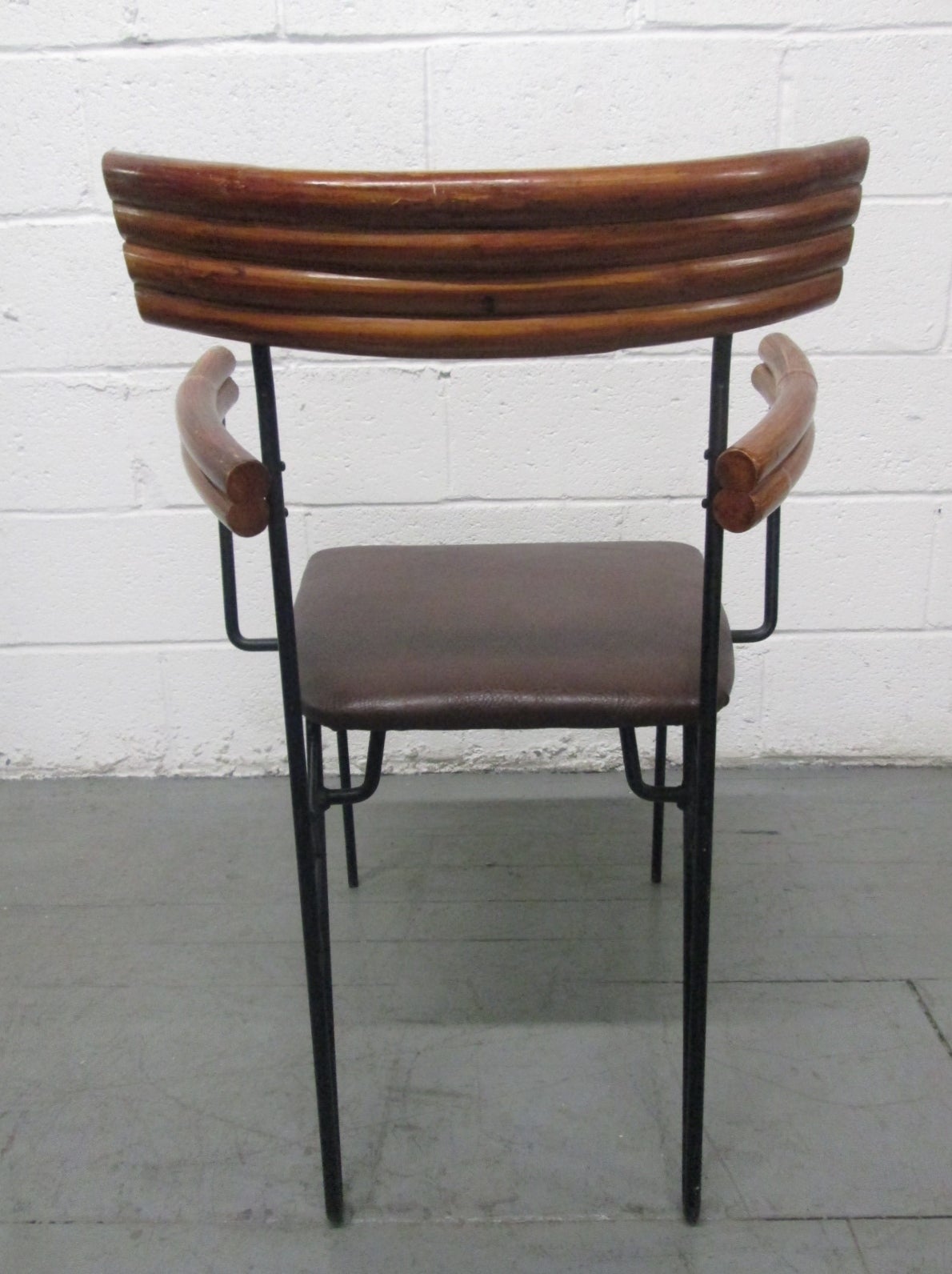 Four 1950s wrought iron and rattan armchairs with leather seats. Has a wrought iron frame with a decorative pattern. Patio Furniture. Bamboo Curved arms. Measure: Arm height is 26.75H. 