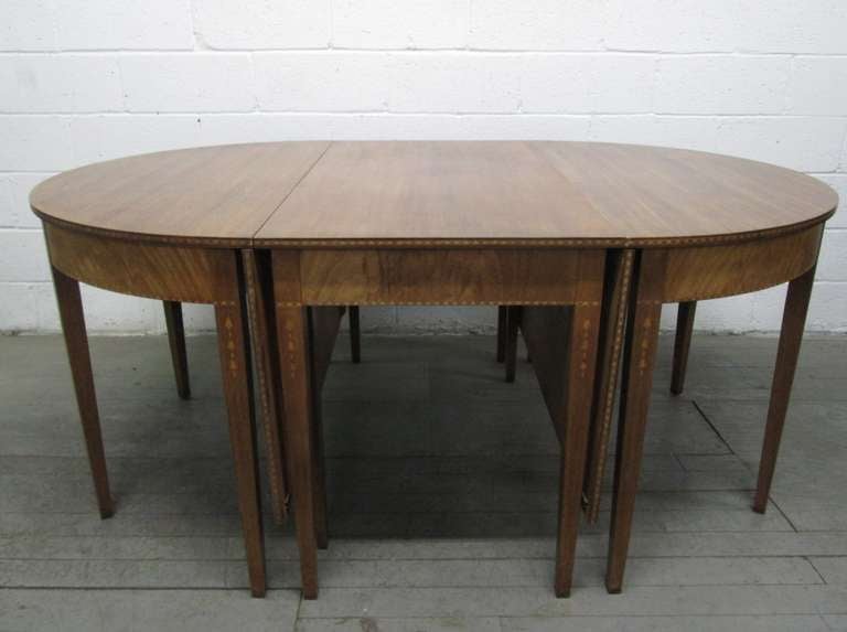 Antique mahogany dining table which converts to a pair of demilune tables, a drop-leaf table and a dining table (extra long).
The table has a beautiful inlay pattern to the sides and legs. Fully extended measures: 115