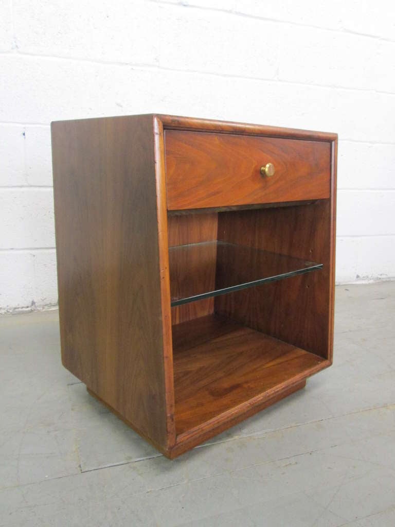 Pair 1960s Drexel nightstands for the Declaration line.  The nightstands are walnut with an adjustable glass shelf and a single pull out drawer.  Has a slanted front.  Measures:  24.5