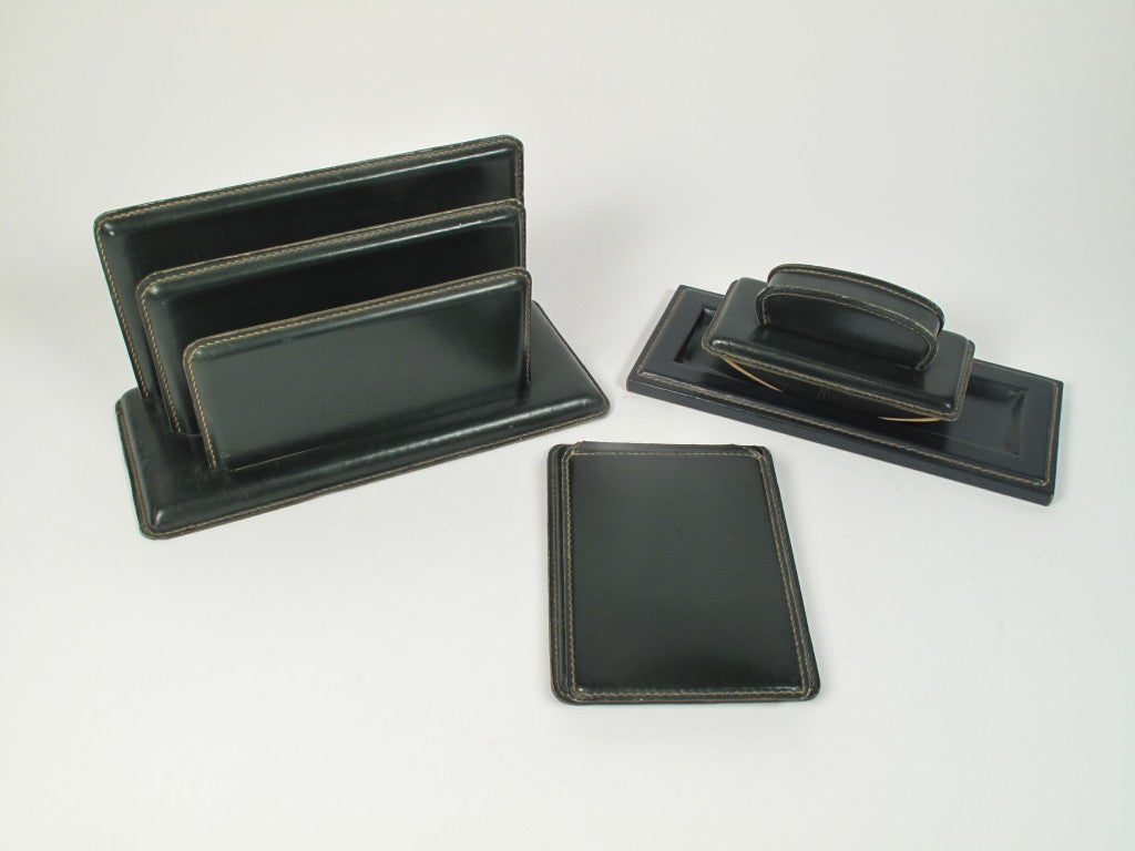 Very nice 4 piece desk set in patinated dark green leather designed by Jacques Adnet and manufactured by Hermes. Set includes a letter holder, note pad holder, ink well and stamp.