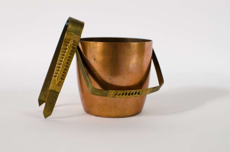 Handsome petite copper and brass ice bucket and tongs with rattan handles designed by Hagenauer c.1940's, Austria. Stunning modernist design. Both pieces signed.

Tongs measure 5.5