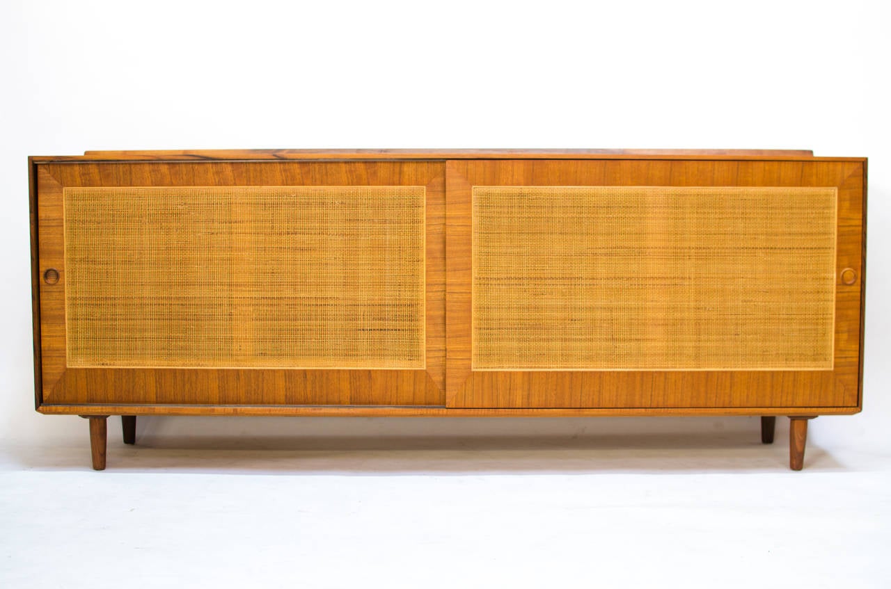 Part of Finn Juhl's 1952 collection of designs for Baker Furniture, this cane-front sideboard is absolutely striking from any angle. Two sliding doors conceal three drawers left, and an adjustable shelf right. The case sits on four tapered legs