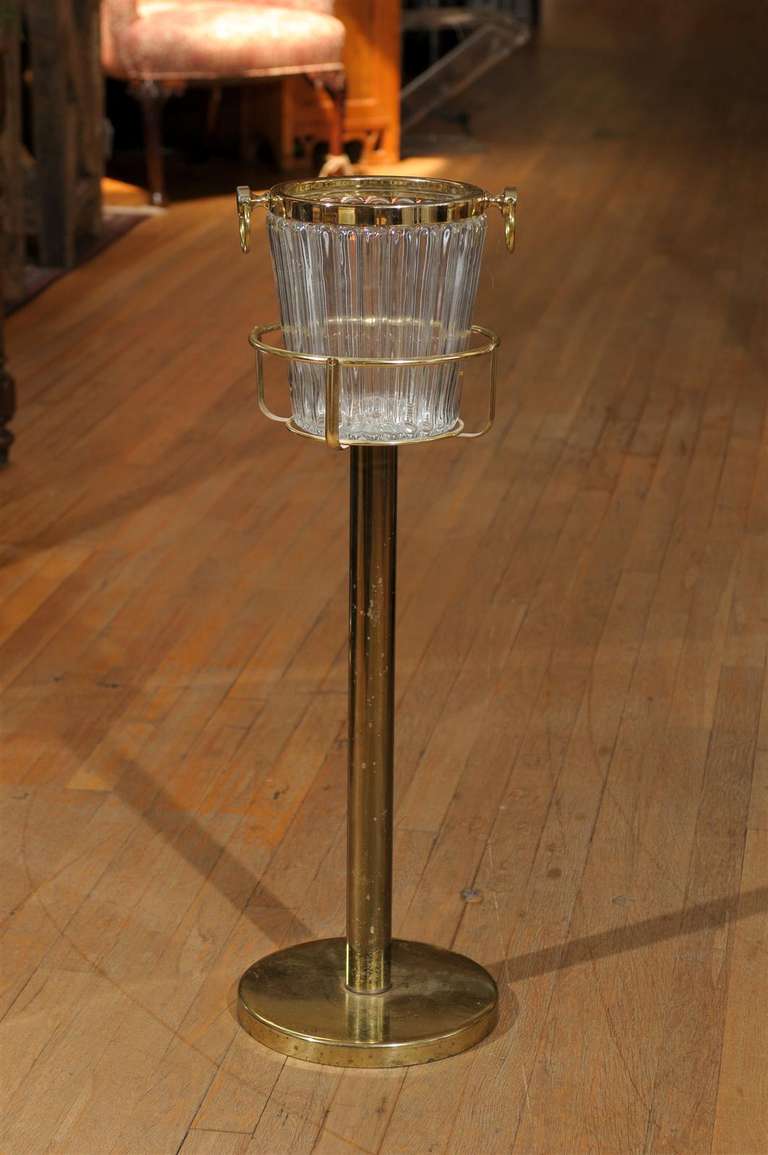 Mid Century fluted glass champagne bucket/ cooler with a fitted brass rim and large brass bail handles on either side and resting on a brass stand.