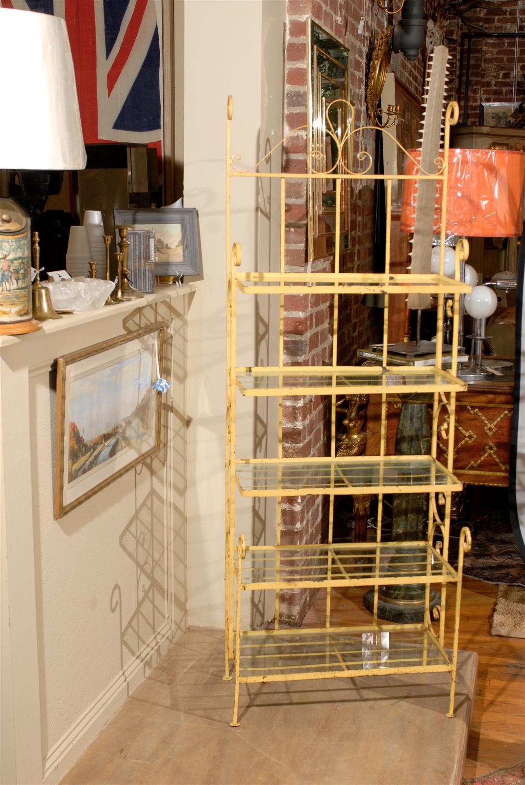Petite midcentury baker's rack having scrolling ironwork in the original yellow paint and supporting five glass shelves.