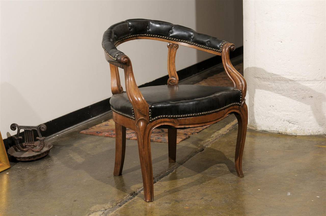Early 20th Century Italian library chair of carved walnut with a tufted black leather barrel back chair rail and black leather seat, all decorated with aged brass nail heads.
