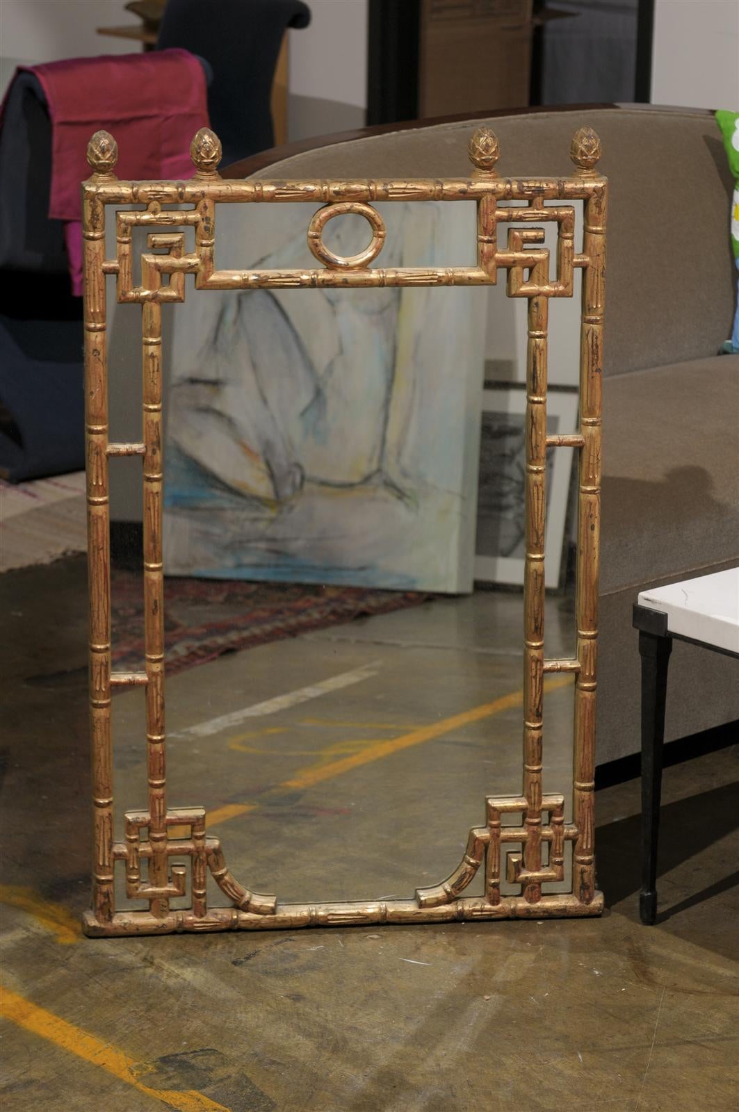 Mid-20th century mirror in the Hollywood Regency style with inset Asian inspired motifs on the carved giltwood bamboo frame and four pineapple finials along the crown.