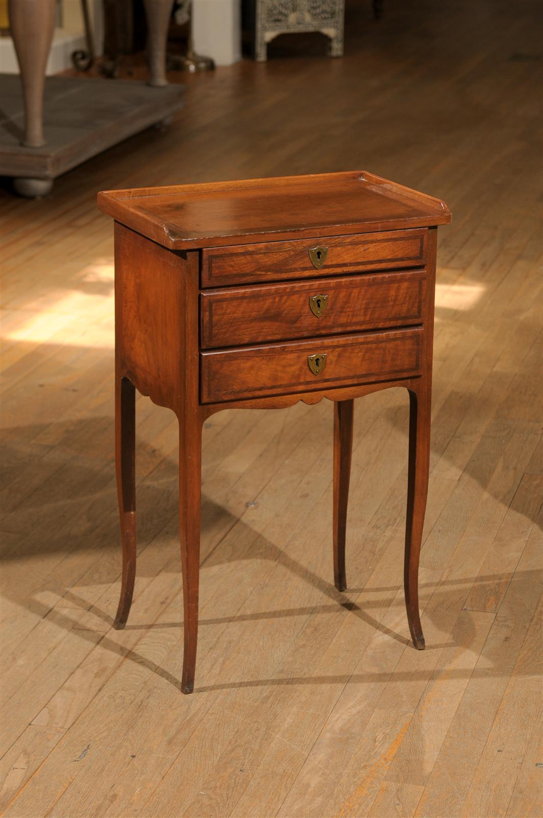 Antique Italian Neoclassical petite side table of walnut with inset inlay on the top, sides, and on the drawers.  The top has a wooden gallery that rests on a case holding three graduated drawers with brass shield escutcheons.  The table's scalloped