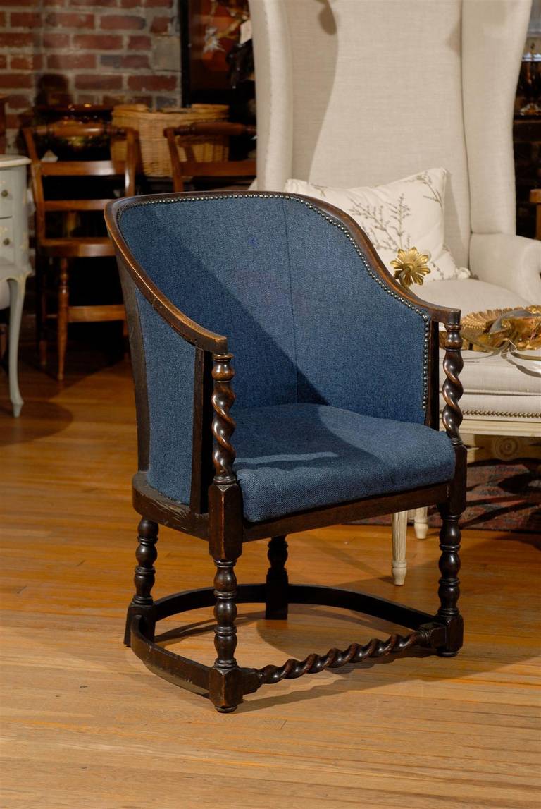19th Century English barrel back chair of oak with upholstered back and seat decorated with nail heads and raised on four turned legs joined by a U-stretcher.   The arm stiles and front stretcher are turned in a barley twist pattern.